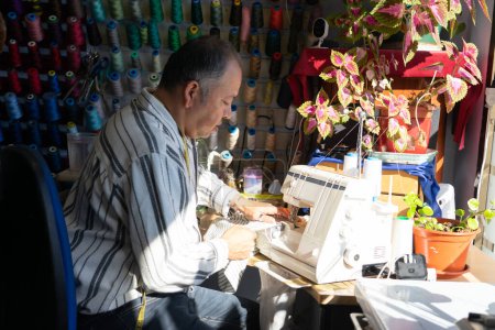 Latino seamstress man sewing with his sewing machine in his small sewing business