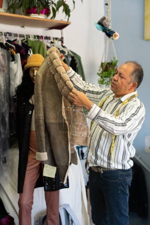 Hombre diseñador de ropa mirando un abrigo de piel en su taller