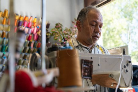 Homme latin de 50 ans cousant avec une machine à coudre dans son atelier de couture