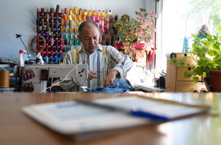 Seamstress man sewing a garment in his sewing shop. 50 year old Latino man working in his small business