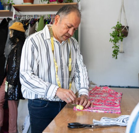 Téléchargez les photos : Homme latino couturière mesurant un tissu dans son atelier de couture - en image libre de droit