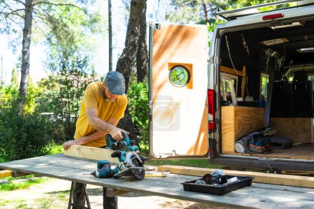 Homme coupant des lattes en bois pour personnaliser son camping-car