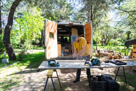 Photo for Man sanding wood to camperize his camper van - Royalty Free Image
