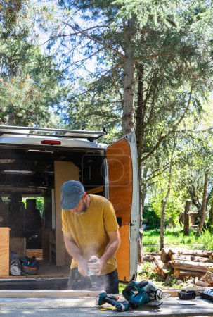 Téléchargez les photos : Homme caucasien ponçage bois pour camper son camping-car à l'extérieur - en image libre de droit