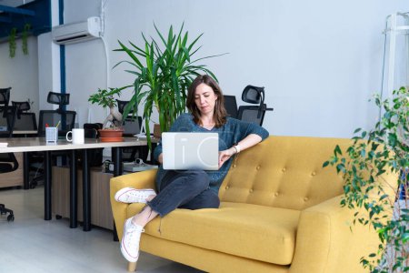 Mujer caucásica trabajando con el ordenador portátil en el sofá en un coworking