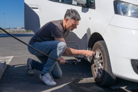 Caucasian man doing maintenance on his van before traveling, inflating the tires