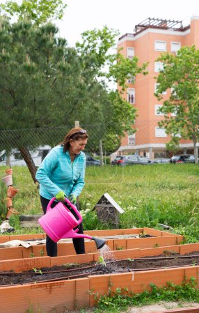 Mujer de 60 años regando un jardín urbano comunitario