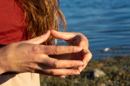 Woman's hands doing the hakini mudra in nature with a lake behind