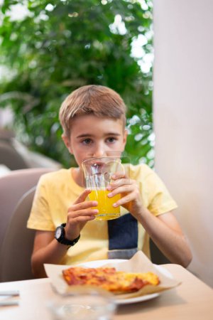 8-jähriger kaukasischer Junge trinkt eine Orangenlimonade
