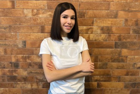 Confident young woman posing with arms crossed against brick all background. portrait of a smiling  girl in the white t - shirt