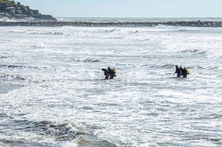 Vier taktische Taucher, Froschmänner, steigen vom Strand ins Meer ein