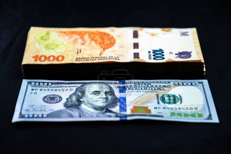 Foto de Comparación de una pila de billetes de 1000 pesos argentinos con un billete de 100 dólares estadounidenses. Inflación. Consecuencias de la cuestión monetaria en Argentina. - Imagen libre de derechos