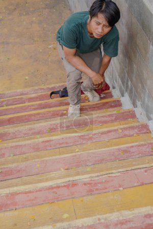 Top view of a handsome man walking up the stairs, bending over and holding the safety railing.