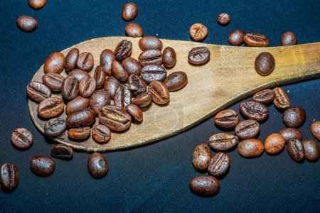Photo for Black coffee beans are seen close up with a wooden spoon on a black cloth. - Royalty Free Image