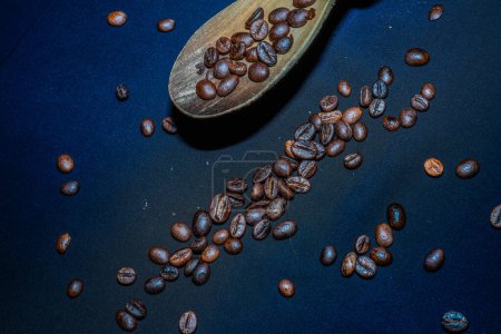 Photo for Black coffee beans are seen close up with a wooden spoon on a black cloth. - Royalty Free Image