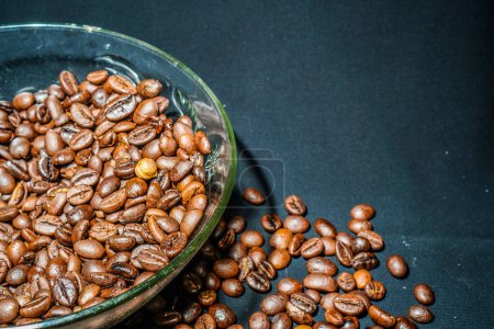 Photo for Black coffee beans in a transparent glass bowl, on a green table. - Royalty Free Image