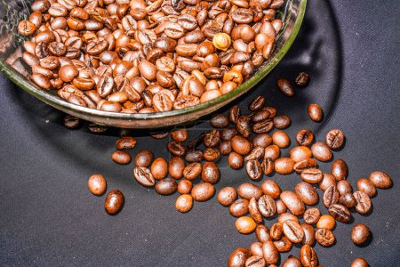 Photo for Black coffee beans in a transparent glass bowl, on a green table. - Royalty Free Image