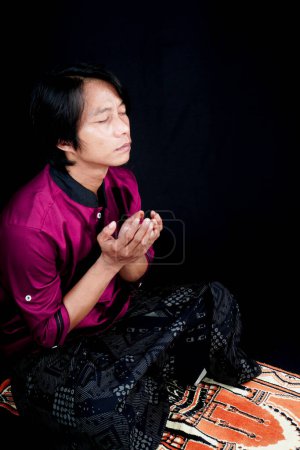 Seitenansicht eines Mannes, der auf einer Gebetsmatte auf schwarzem Hintergrund betet.