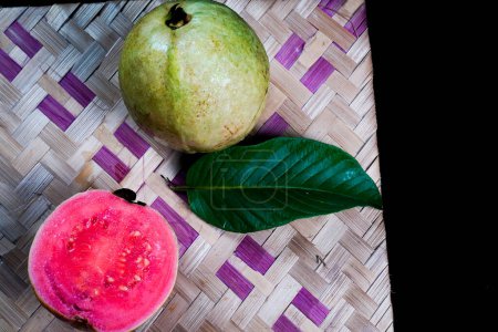 Guave isoliert. Kollektion von rotfleischigen Guaven mit gelbgrüner Schale und Blättern auf schwarzem Hintergrund mit gewebtem Bambus.