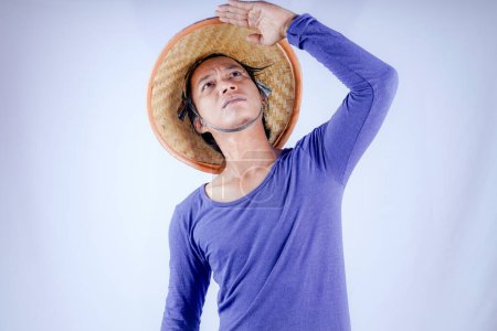 Javanese man wearing a woven bamboo hat is looking up on a white background with empty space for advertising.