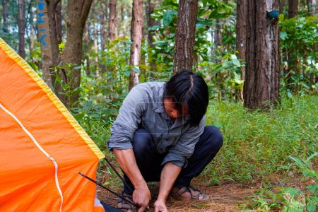 Javanese man is setting up a tent in a rubber forest, the concept of recreation in the forest