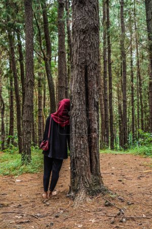 vue arrière d'une femme portant un foulard appuyé contre un arbre en caoutchouc dans la forêt seule.