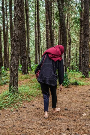 rear view of a woman wearing a headscarf playing alone in the rubber forest.