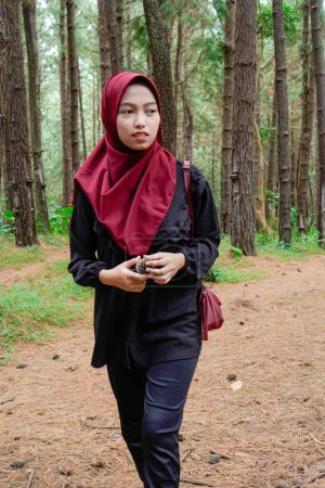 a woman wearing a headscarf is walking alone in the forest, against the backdrop of trees.