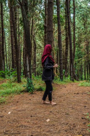 rear view of a woman wearing a headscarf playing alone in the rubber forest.