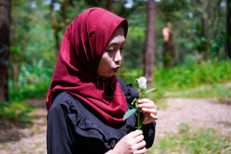 Mujer musulmana está tratando de soplar flores de diente de león en medio de un bosque de caucho.