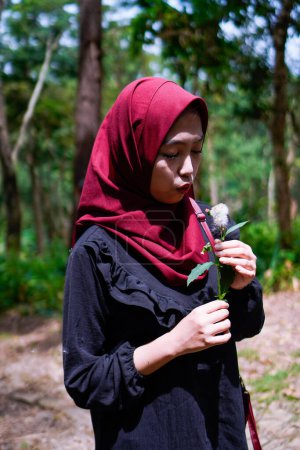 Mujer musulmana está tratando de soplar flores de diente de león en medio de un bosque de caucho.
