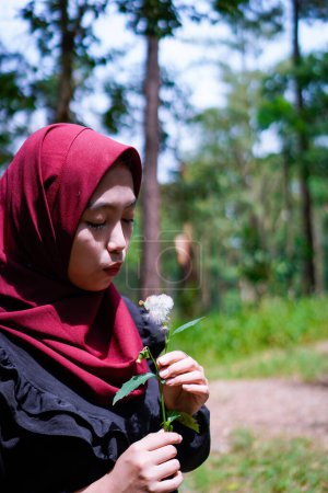 Muslim woman is trying to blow dandelion flowers in the middle of a rubber forest.