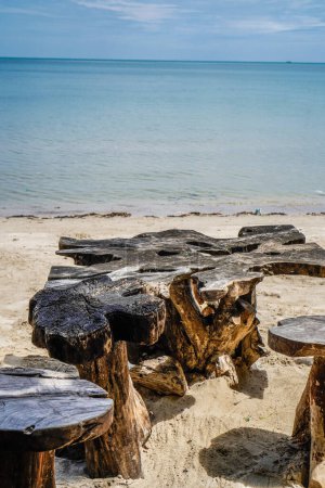 An antique wooden table and chairs on the beach sand with a backdrop of the blue sea with empty advertising space.
