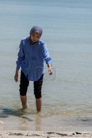 Asiatin im Hijab spielt am Strand vor hellem Himmel mit leerer Werbefläche.