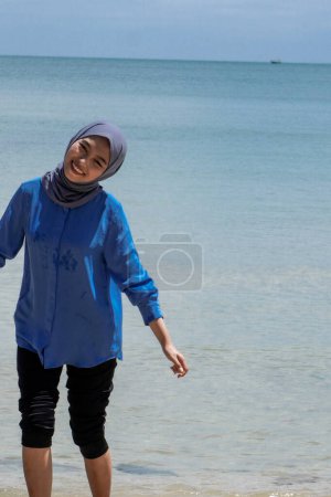 Asian woman in hijab is playing on the beach against a bright sky background with empty advertising space.