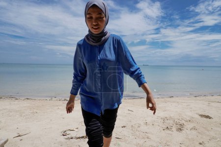 Asiatin im Hijab spielt am Strand vor hellem Himmel mit leerer Werbefläche.