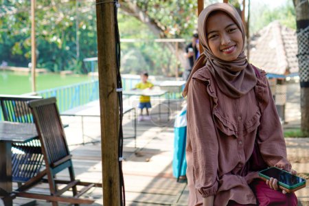 Javanerin im Hijab sitzt mit lächelndem Gesichtsausdruck im Park, Sommerferienkonzept.