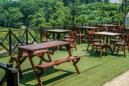 benches with integrated tables are placed in an open space for cafe visitors, with a forest background.