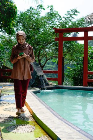 Muslimische Frau läuft neben dem Schwimmbad und hält ihr Handy in der Hand.