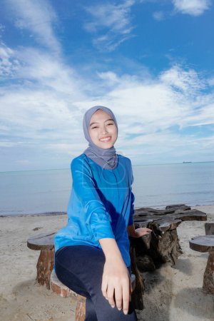 schöne Muslimin sitzt am Strand und blickt in die Kamera, der Hintergrund ist ein klarer Himmel mit leerem Kopierraum