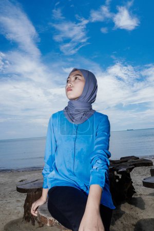 Muslimische Frau sitzt am Strand mit dem Gesicht nach oben, gegen den Himmel als Hintergrund mit leerem Raum zum Kopieren.