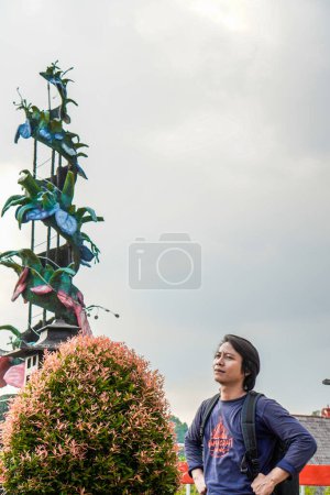 Javanese man is standing with a backpack on his shoulders against a cloudy sky with free space for photocopying.