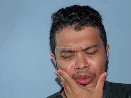 Der Gesichtsausdruck eines asiatischen Mannes, wenn er Zahnschmerzen hat