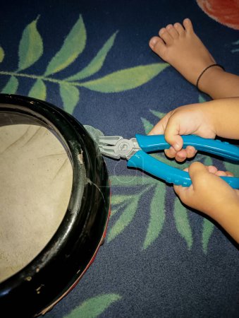Small children play with a toy craftsman's tool in the form of pliers