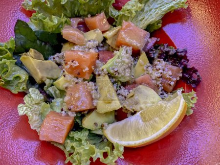 Salmon salad with quinoa and avocado on a red plate.
