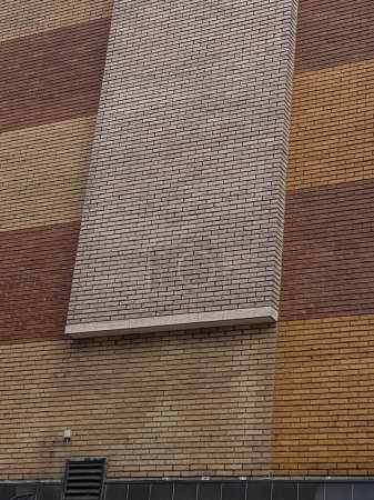 A brick wall of a modern building with a vertical rectangular window laid with bricks