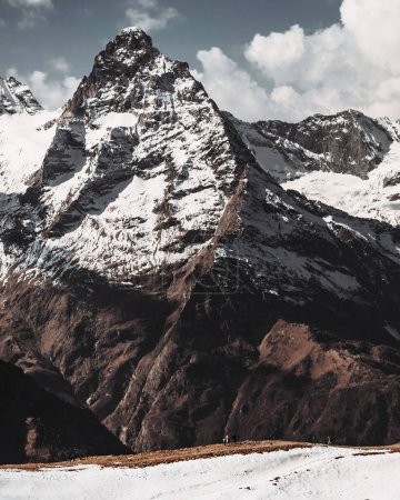 Photo for Vertical shot of a mountain covered with snow. Black peak in white snow, gray sky, autumn, winter, brown, red earth. Dombay. Low angle shot. - Royalty Free Image