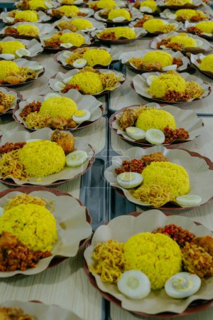 Nasi Kuning oder Gelber Reis in einem Teller. In Indonesien genannt "Nasi Tumpeng" Ein festliches indonesisches Reisgericht mit Beilagen. Tumpeng Reis in einem Teller auf dem Tisch.