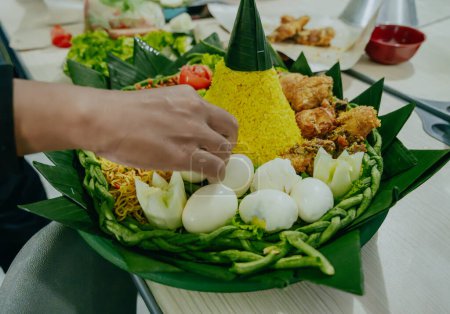 Process of decorating yellow rice in a cone shape. In Indonesia called "Nasi Tumpeng" A festive Indonesian rice dish with side dishes. Tumpeng rice in green plastic tray. 