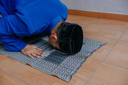 Asian muslim man praying and prostrating on prayer mat in mosque.